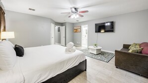 Habitación de hotel moderna con una cama grande, un ventilador de techo, un televisor de pantalla plana, un sofá y una mesita con una planta.