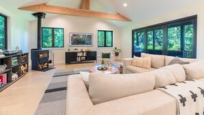 A spacious living room with a large sofa, a fireplace, and large windows offering a view of the outdoors.