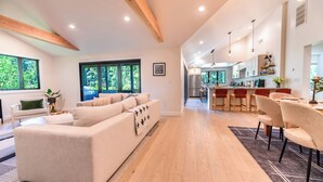 A modern living room with a sofa, a dining area with chairs, and a kitchen with a refrigerator.