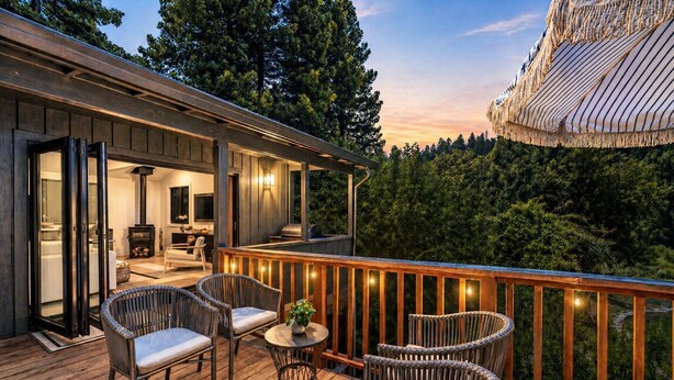 A wooden deck with wicker furniture, a grill, and a cozy interior with a fireplace.