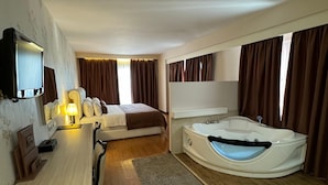 Habitación de hotel con cama, escritorio con lámpara, televisión y una bañera grande, además de cortinas.