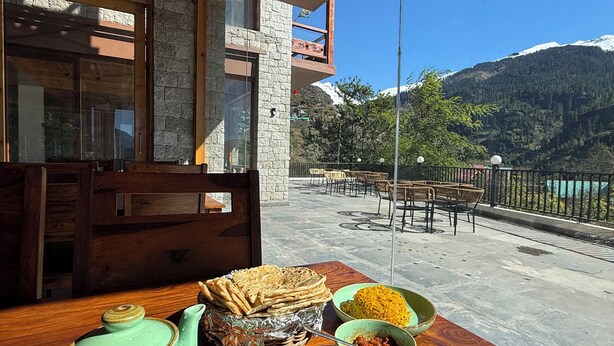 A dining table with a teapot, cups, and bowls set outdoors with a mountain view. - Rigzin House by Meghsparsh Resorts (Manali)