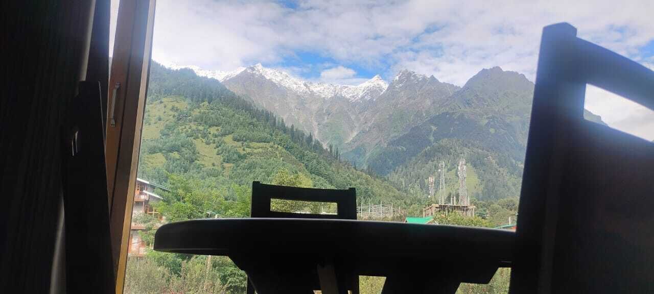 Une vue depuis une fenêtre, donnant sur un paysage de montagne, avec des sommets enneigés et une végétation luxuriante.