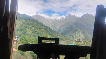 Une vue depuis une fenêtre, donnant sur un paysage de montagne, avec des sommets enneigés et une végétation luxuriante.