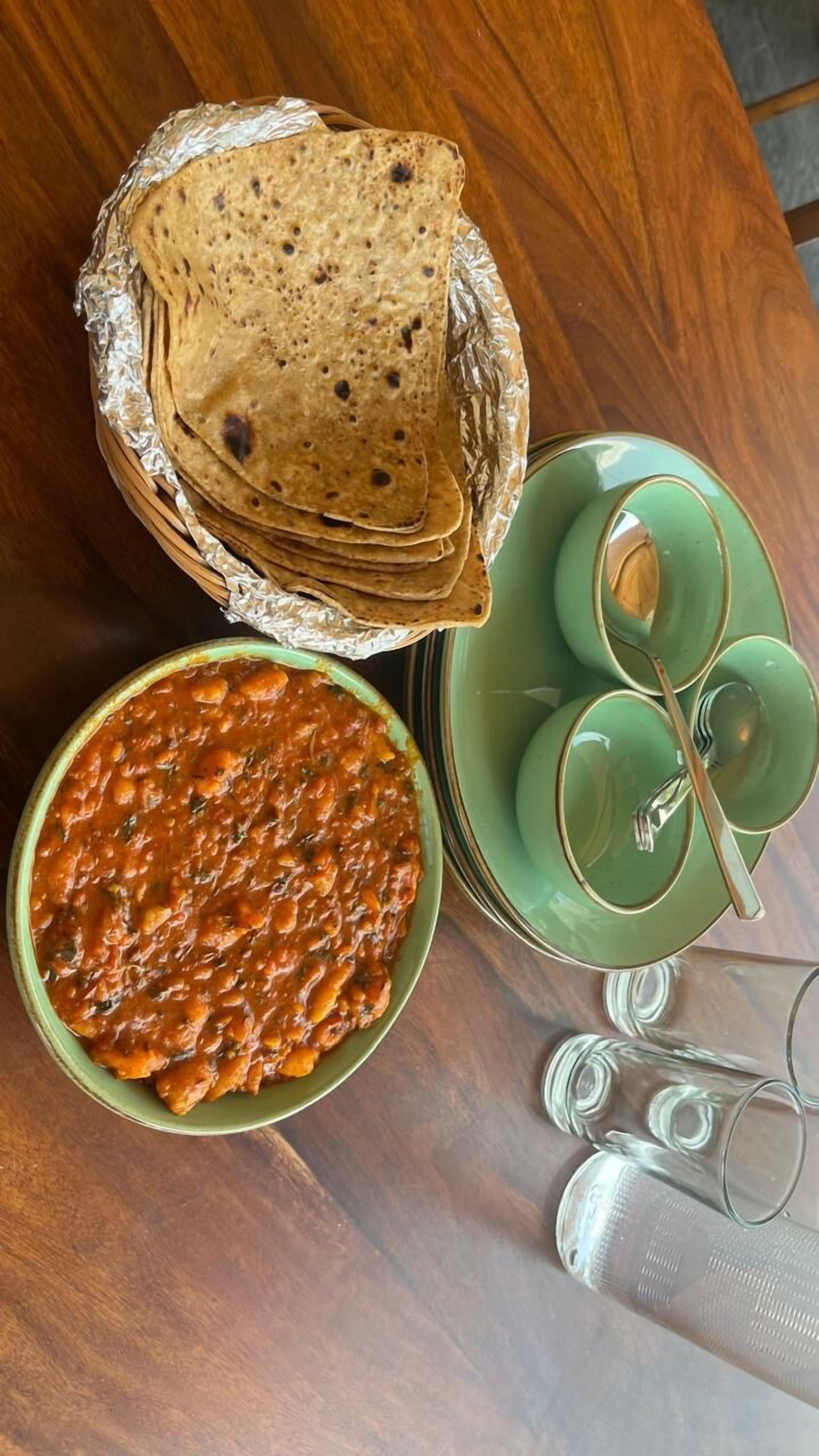 Una mesa con una cesta de panes planos, un tazón de chili y un juego de tazas y platillos verdes.