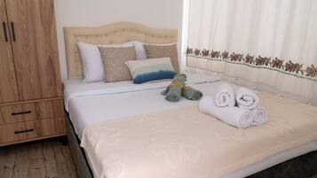 A neatly made bed with a beige headboard, a white blanket, and rolled towels.
