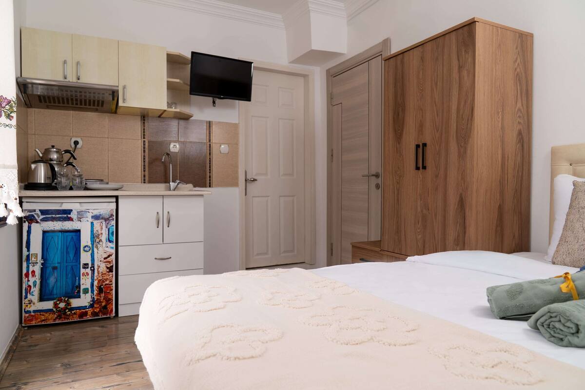 Una habitación de hotel con cama, armario, televisor y kitchenette.