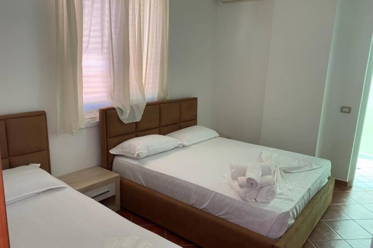 Habitación de hotel con una cama individual, una mesita de noche y un ventanal con cortinas traslúcidas.