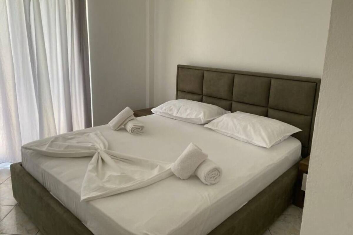 Una cama bien hecha con sábanas y almohadas blancas, un cabecero acolchado y una toalla enrollada sobre la cama.
