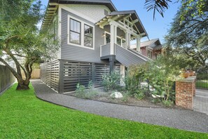 A two-story house with a grey exterior, a wooden deck, and a brick wall.