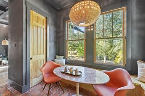 A room with a large window, a round table with chairs, and a wicker chandelier.