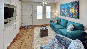 Un salon moderne avec un canapé de couleur turquoise, un fauteuil à motifs, une table basse et un tableau représentant des poissons accroché au mur.