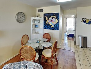 Un comedor con una mesa redonda, sillas de mimbre y un reloj en la pared.