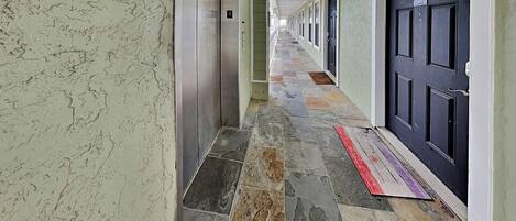 A hallway with a tiled floor, a row of doors, and an elevator.