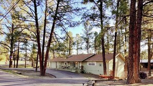 A single-story house with a porch, surrounded by tall pine trees. - Mountain Sage Retreat | Great Location, Fenced Yard (Ruidoso)