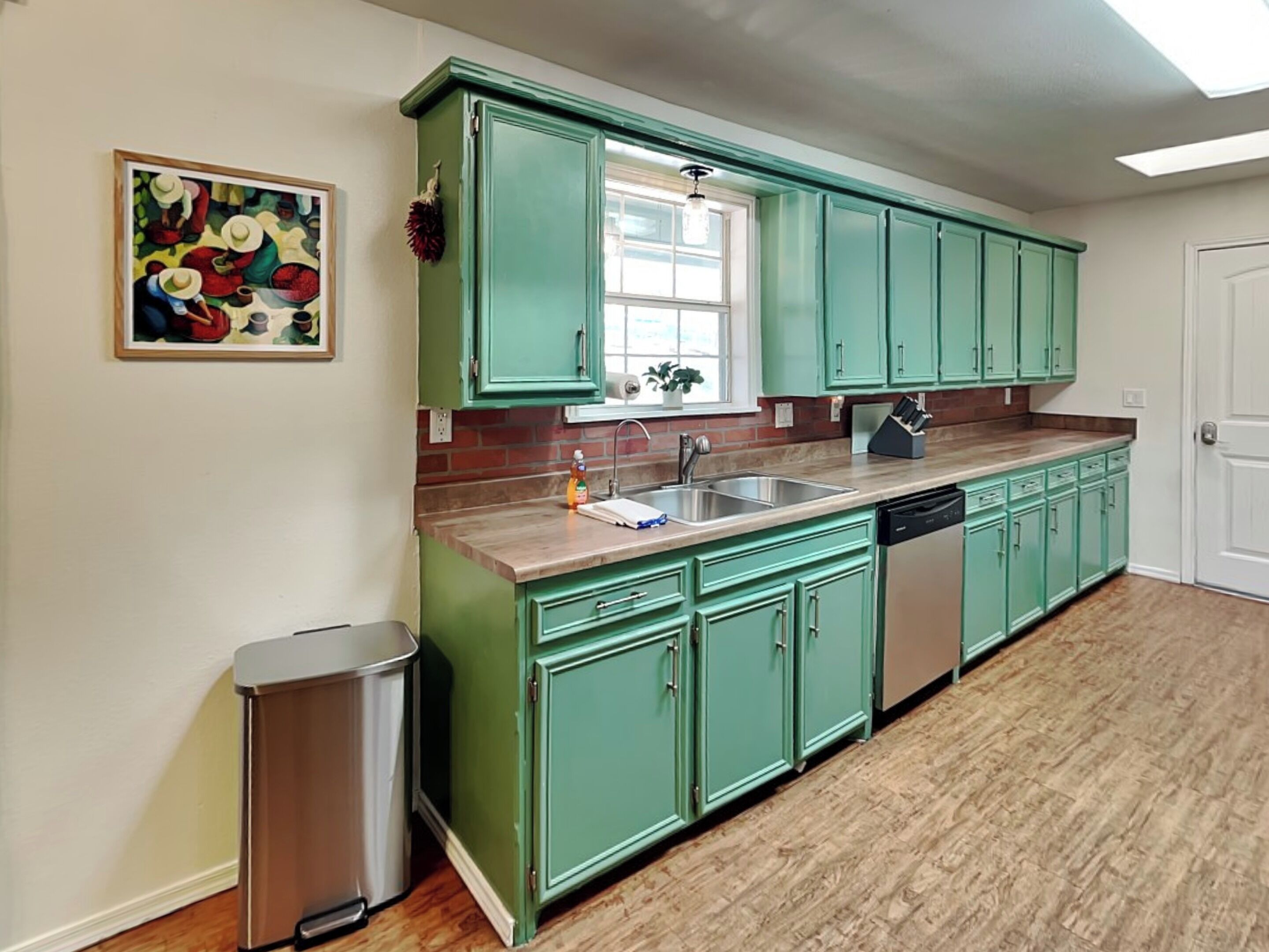 A kitchen with green cabinets, a stainless steel sink, and a dishwasher.