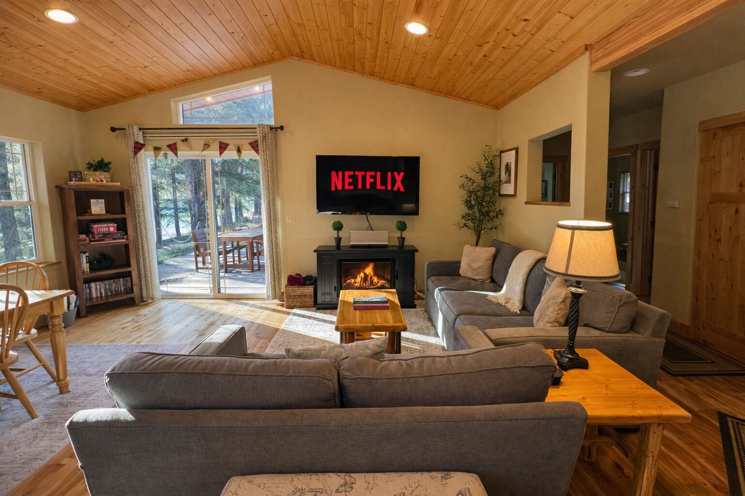 A cozy living room with a fireplace, a sofa, a TV displaying 'NETFLIX,' and a bookshelf.