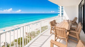 A balcony with a view of the beach and ocean, wooden furniture, and a white railing. - Phoenix Gulf Shores Ii 1203 3 Bedroom Condo (Gulf Shores)