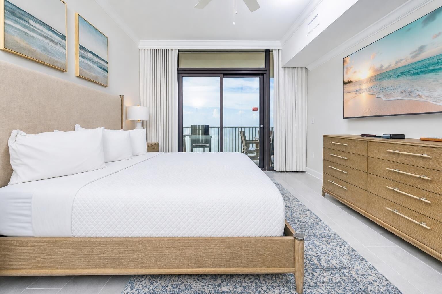 Et hotelværelse med en stor seng, en trækommode, en balkon med stole og et maleri på væggen.