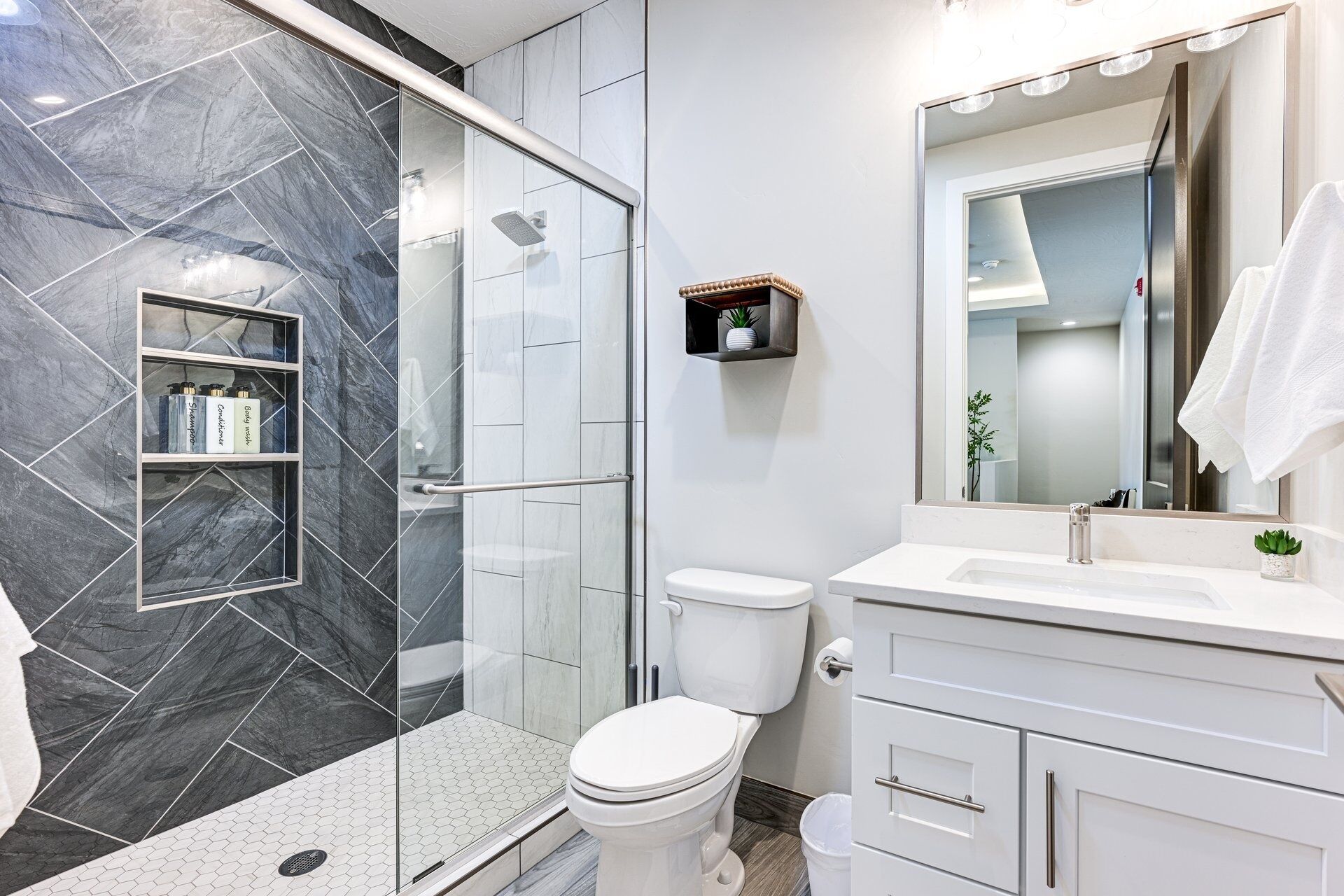 A modern bathroom with a glass shower enclosure, a white toilet, and a vanity with a mirror.