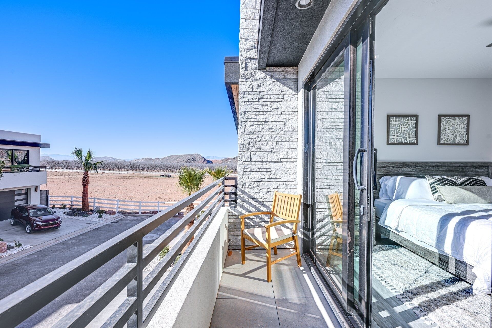 A balcony with a view of a desert landscape, a bed with a striped pillow, and a car parked outside.