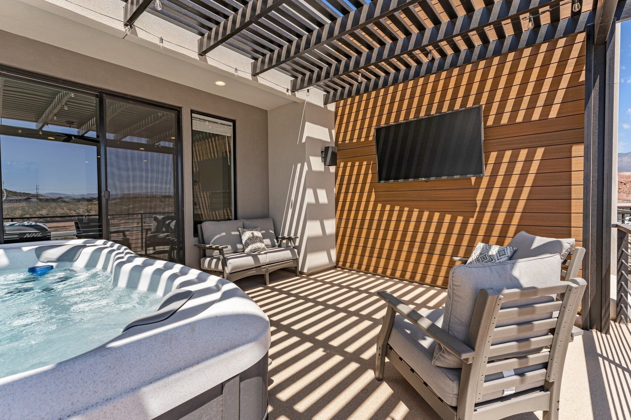 Een terras op het dak met een jacuzzi, lounge stoelen en een televisie bevestigd aan een houten wand.