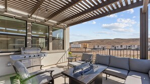 Un patio al aire libre con una parrilla, asientos y vistas a un paisaje desértico.