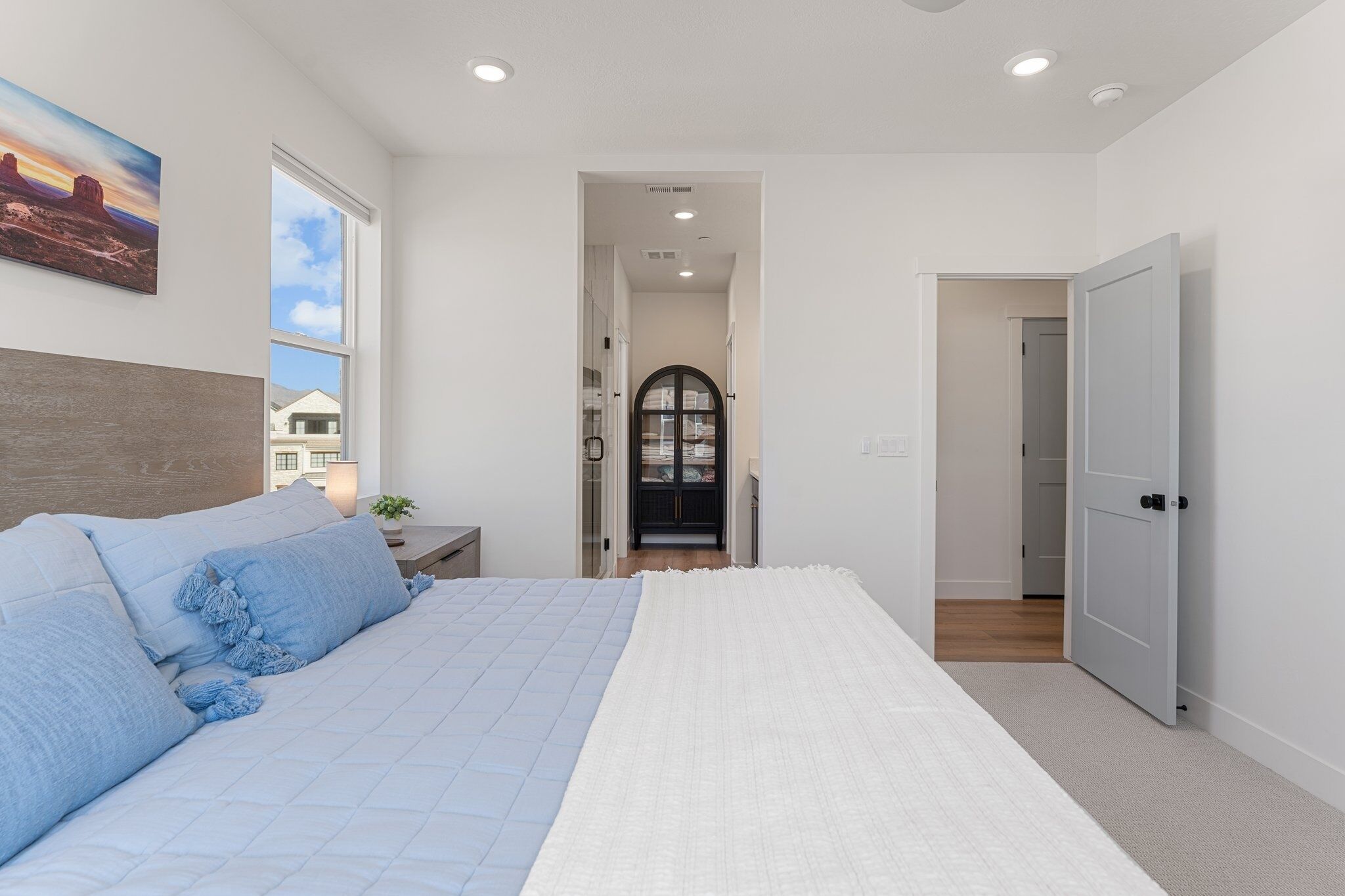 A bedroom with a bed, a nightstand, a window, and a door leading to another room.