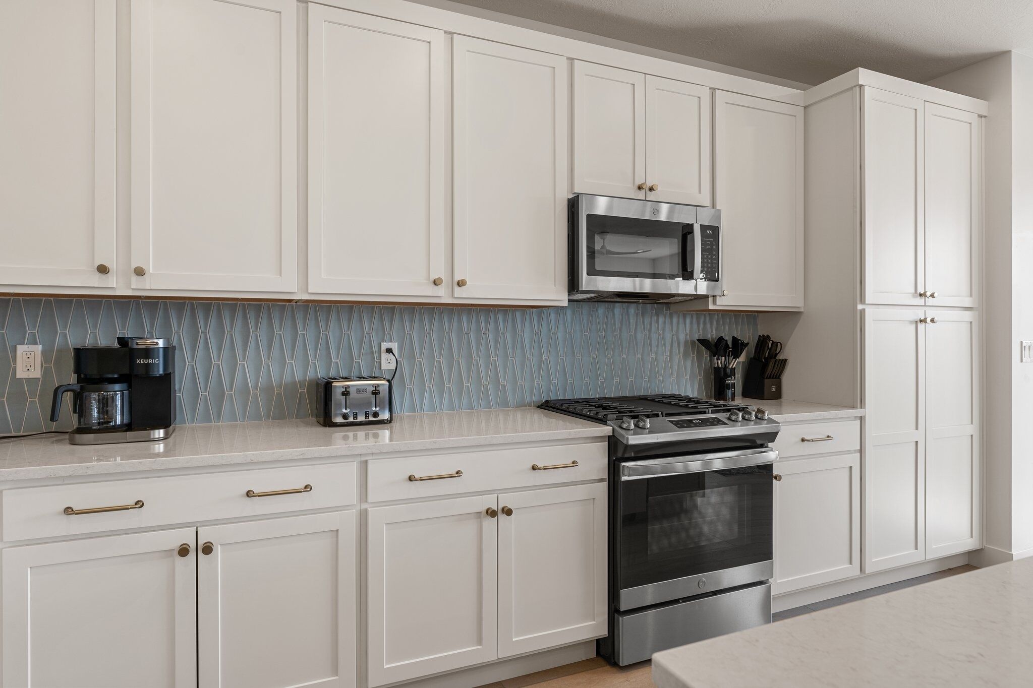 A kitchen with white cabinets, a microwave, a coffee maker, and a stove.