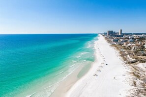 A coastal cityscape with a wide beach, clear blue waters, and a dense urban area with high-rise buildings.