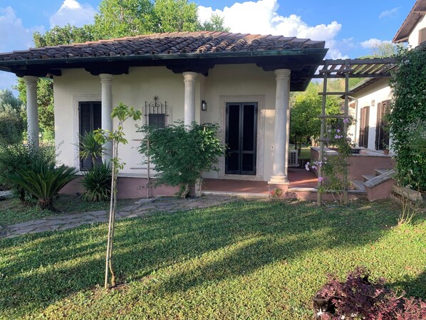 A traditional house with a tiled roof, white columns, and a small garden with grass and plants.