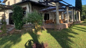 A two-story house with a covered patio area, outdoor seating, and a garden with various plants and a tall tree. - Villa il Turchetto, country house with swimming pool 2km from Terme di Saturnia (Saturnia)