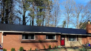 A single-story brick house with a red door, a garage, and a small front yard with grass and a garden hose. - 3-bedroom bungalow in charming Smyrna with WiFi, AC (Smyrna)