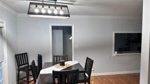 A dining area with a rectangular table, six chairs, a chandelier, and a window with a view of a bookshelf. - 3-bedroom bungalow in charming Smyrna with WiFi, AC (Smyrna)