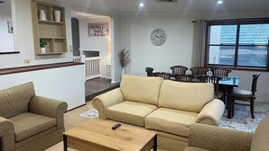 Un salon avec un canapé beige, une table basse et un coin repas comprenant des chaises et une table en bois.