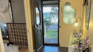 Un couloir doté d’un plancher en bois foncé, d’une porte décorative avec un panneau de verre et d’un vase rempli de fleurs, posé sur un piédestal.