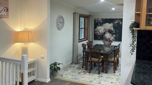 Un coin repas avec une table et des chaises en bois, une horloge au mur et une fenêtre avec des rideaux.