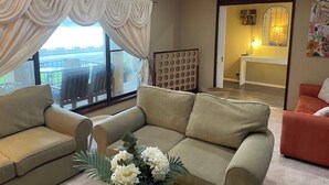 Un salon avec un canapé beige, un fauteuil rouge et une grande fenêtre avec des rideaux.
