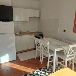 Een kleine keuken met witte kastjes, een inbouwoven, een spoelbak en een eettafel met stoelen.