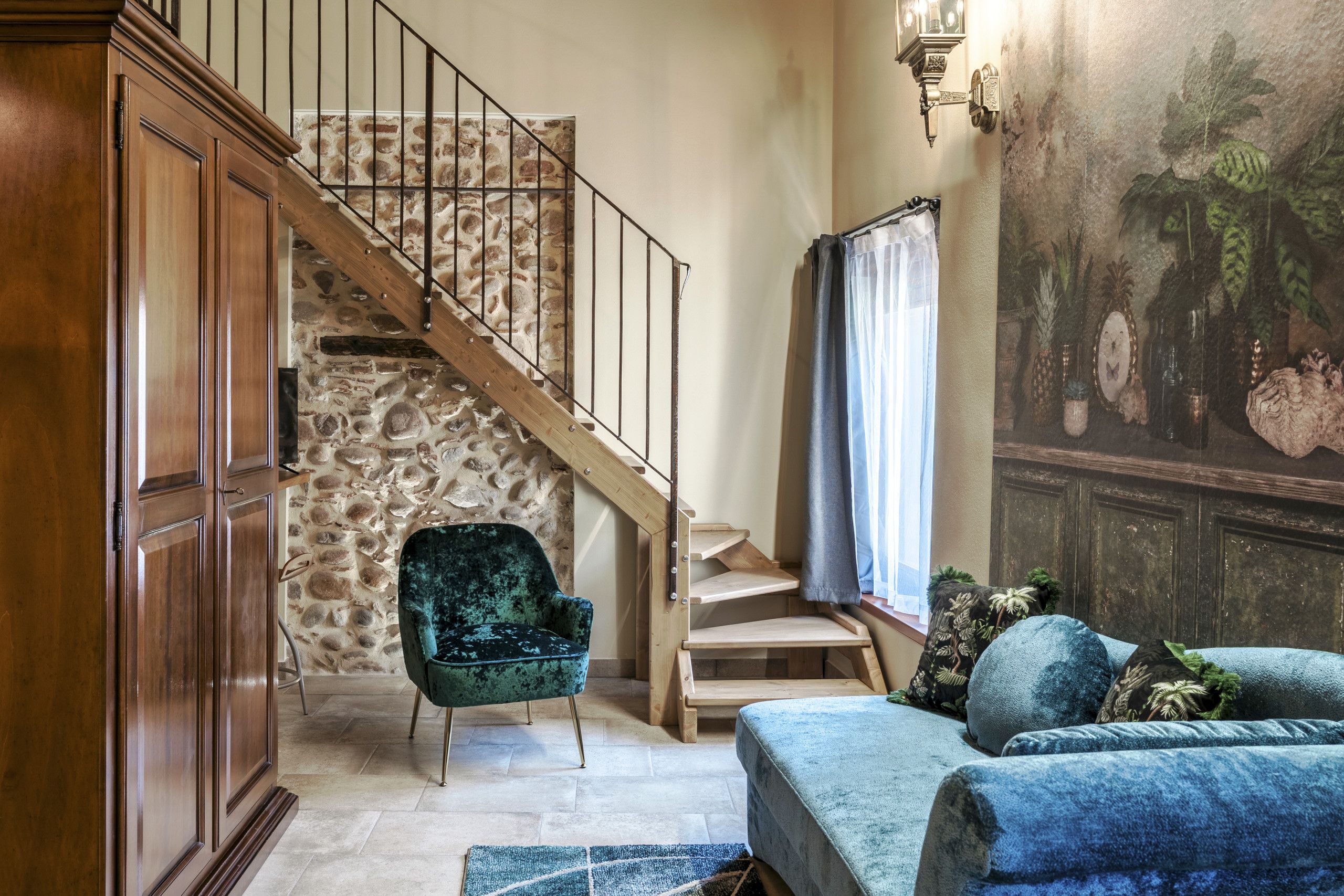 Eine Treppe mit einer Steinsäule, einer Holztür, einem grünen Sessel, einem blauen Sofa und Wandbild.