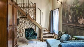 Eine Treppe mit einer Steinsäule, einer Holztür, einem grünen Sessel, einem blauen Sofa und Wandbild.