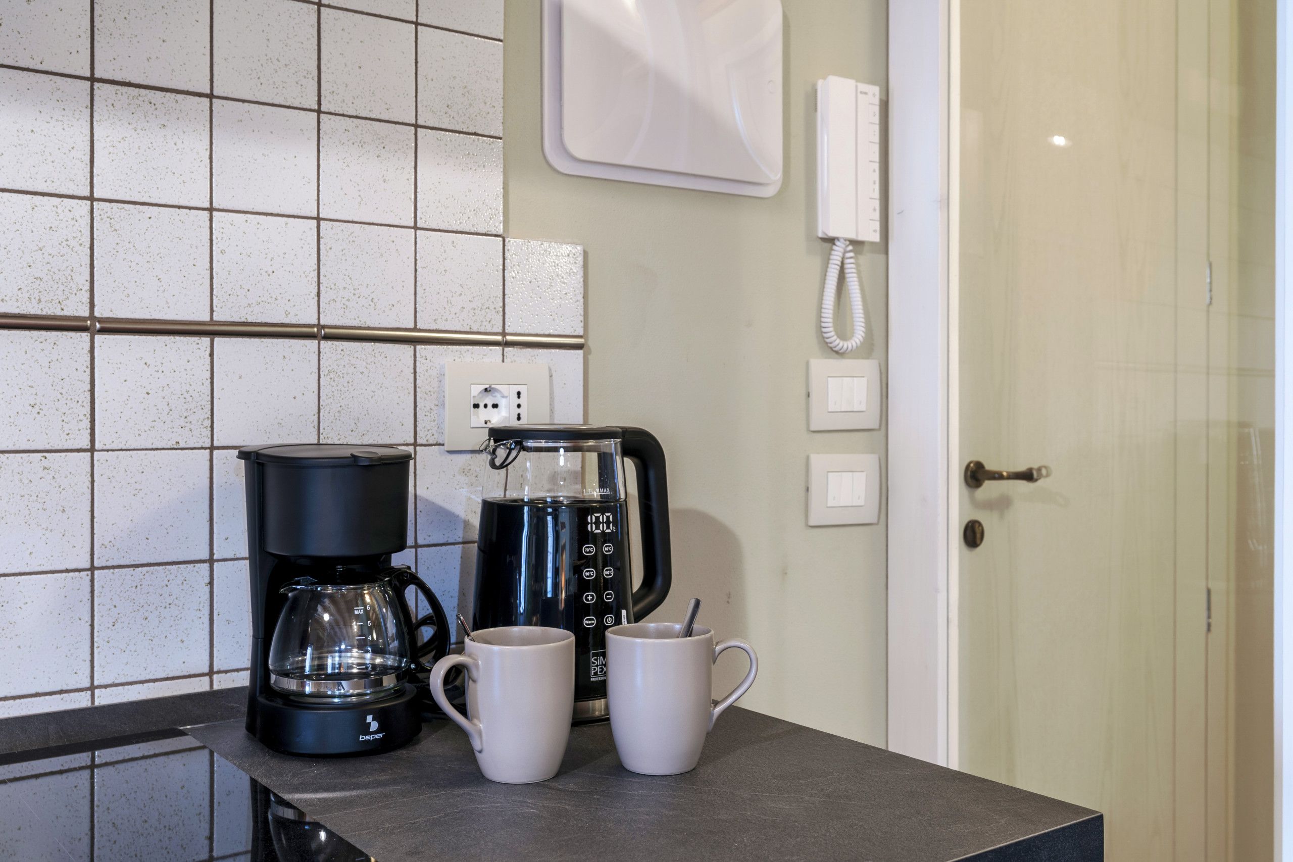A kitchenette with a coffee maker, two white mugs, and a phone on the wall.
