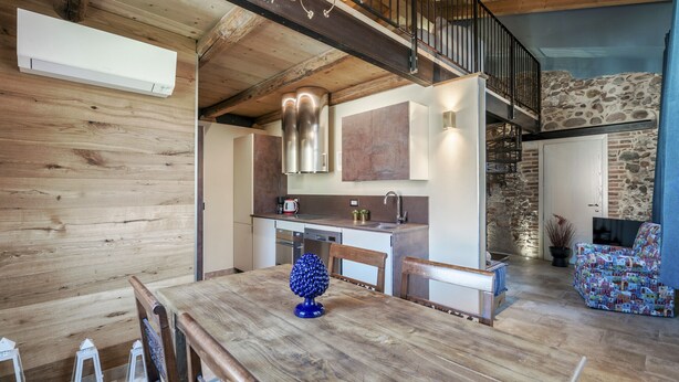 A spacious kitchen with a wooden ceiling, a stone wall, and a dining area with a wooden table and chairs.