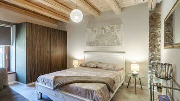 Ein Schlafzimmer mit einem Bett, Nachttischlampen, einem Glastisch, einem Stuhl und einer Steinwand.
