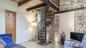A living room with a spiral staircase, a sofa, a TV, and a potted plant.