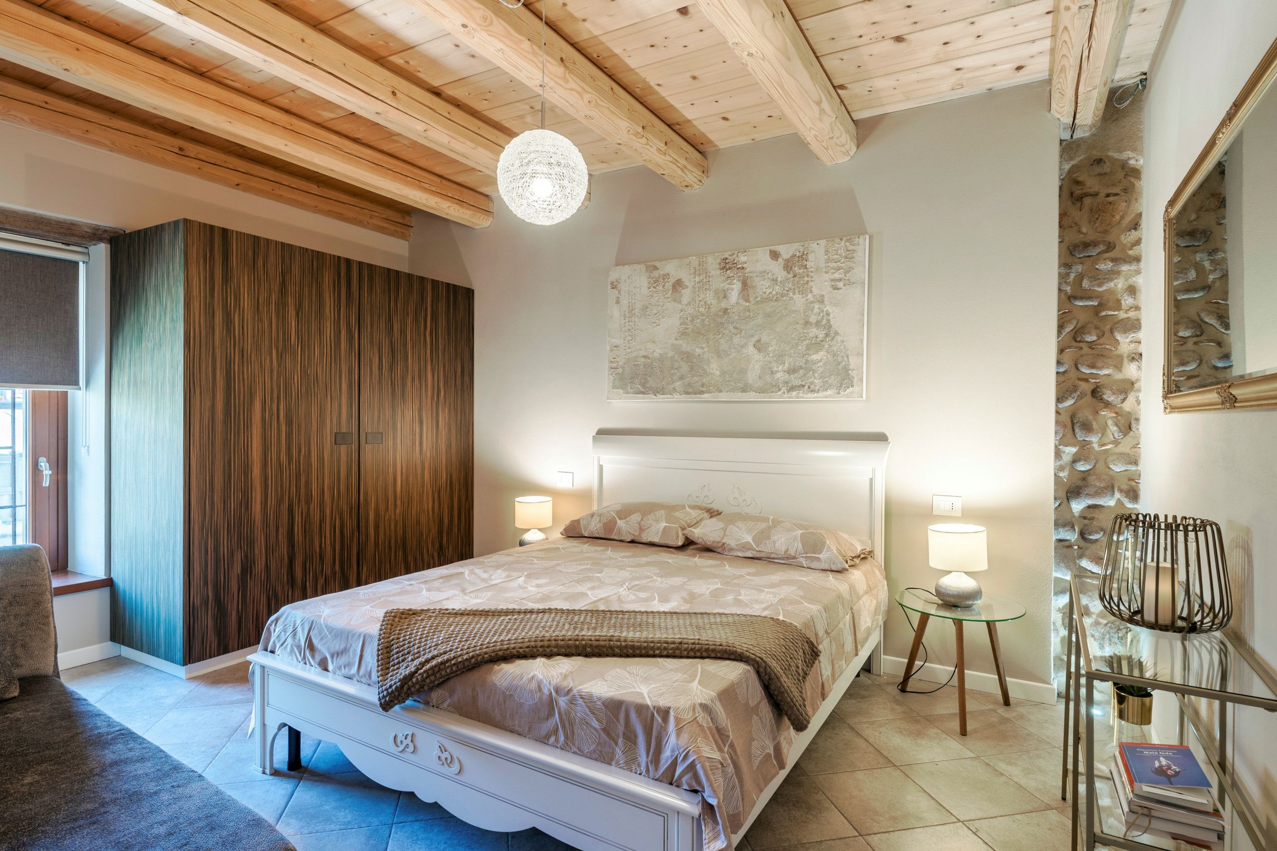 Une chambre à coucher avec un lit, des lampes de chevet, une œuvre d’art accrochée au mur et un mur en pierre.