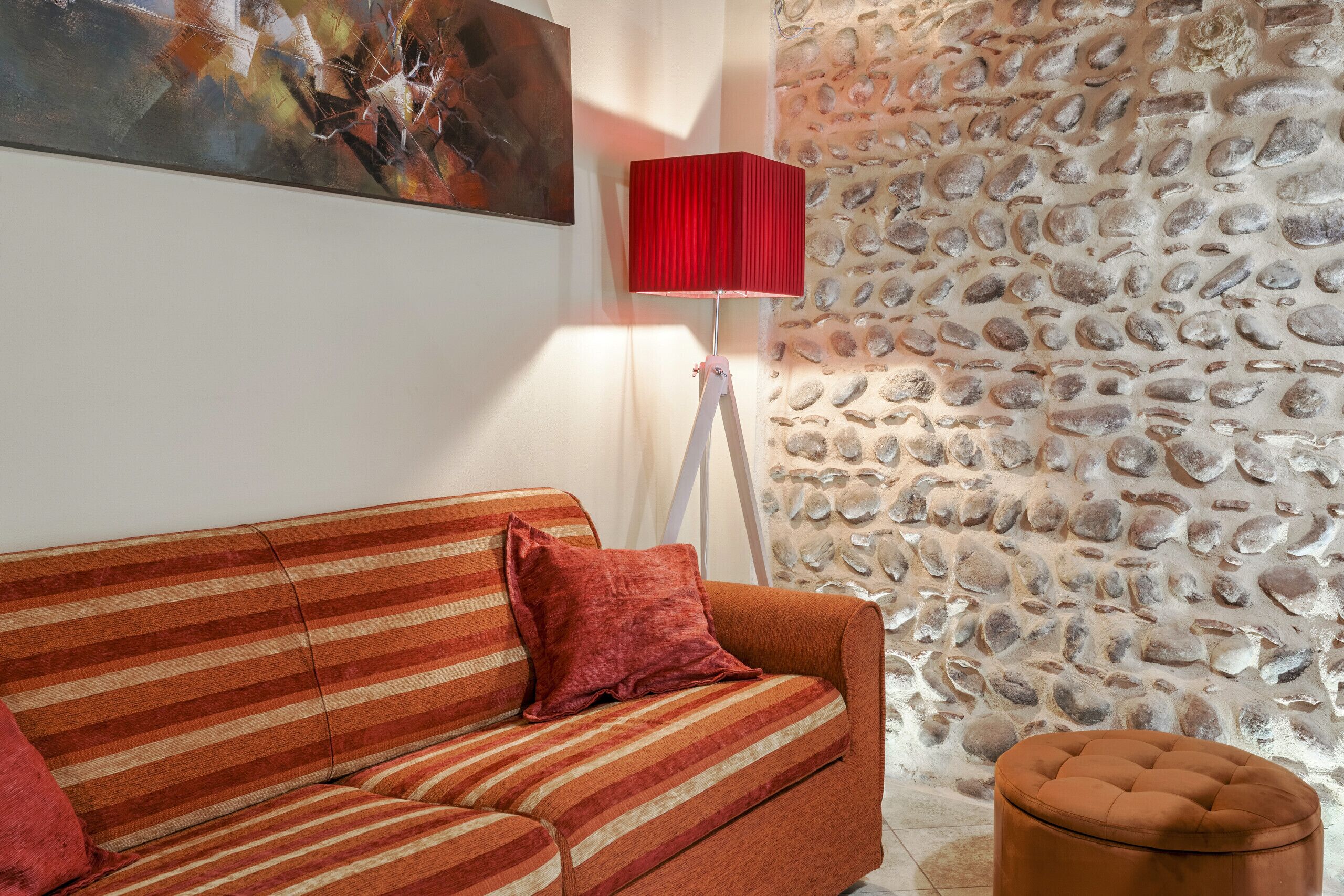 Una habitación con un sofá a rayas, una lámpara roja y una pared de piedra.