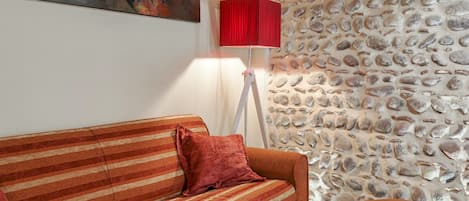 Una habitación con un sofá a rayas, una lámpara roja y una pared de piedra.