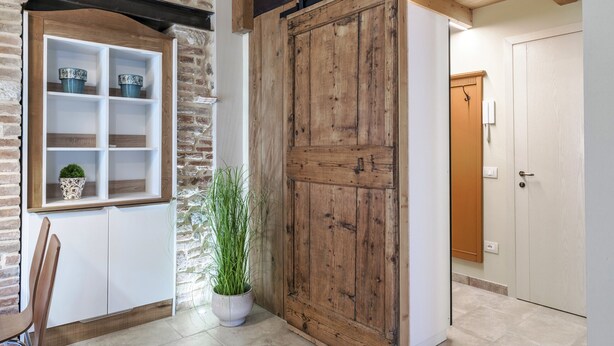Un interno rustico con parete in pietra, porta in legno e un armadietto bianco con ripiani.