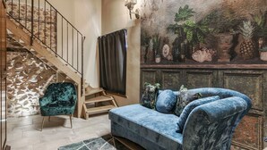 Una stanza con una scala in legno, un divano in velluto blu e un murale con piante tropicali.